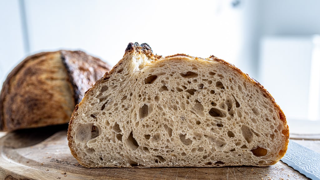 A halved sourdough loaf showing an open, glossy crumb on a wooden board